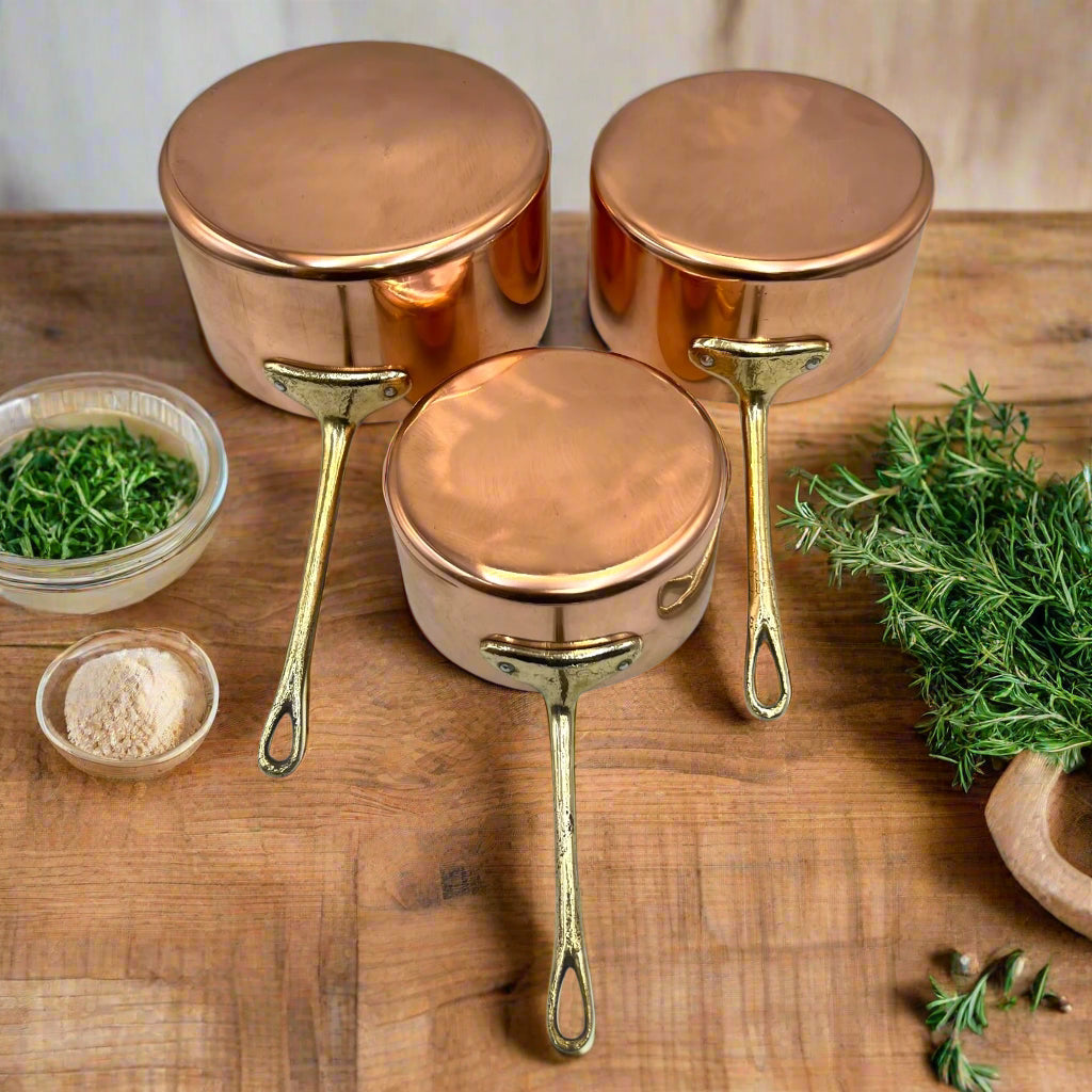 French Copper Pan Set, 3 Copper Saucepans with brass handles on a wooden kitchen table with herbs 