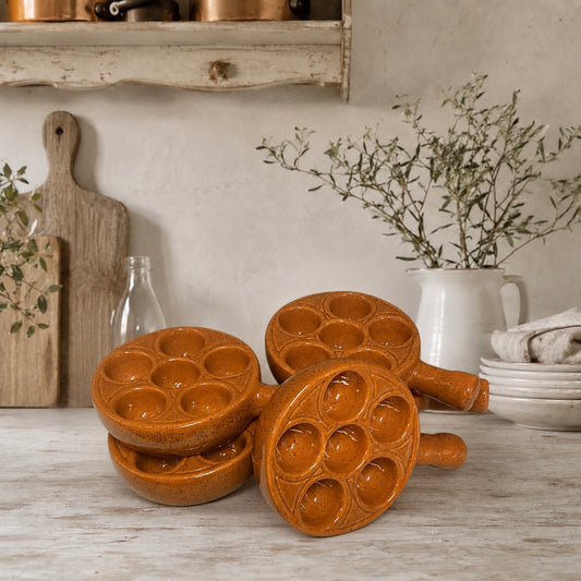 A set of five vintage French brown ceramic escargot plates, perfect for a farmhouse or country-style kitchen, displayed on a rustic counter with a white wall and greenery in the background.