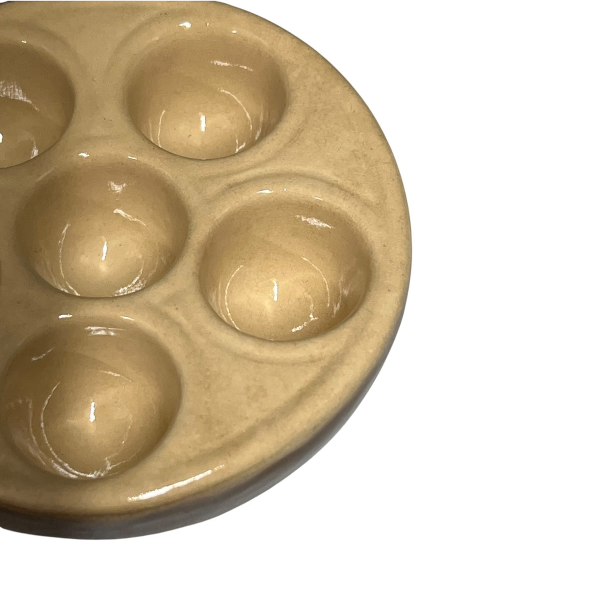 A close-up of a round ceramic escargot bowls with 6 wells, featuring a glossy, warm beige glaze on a plain white background.
