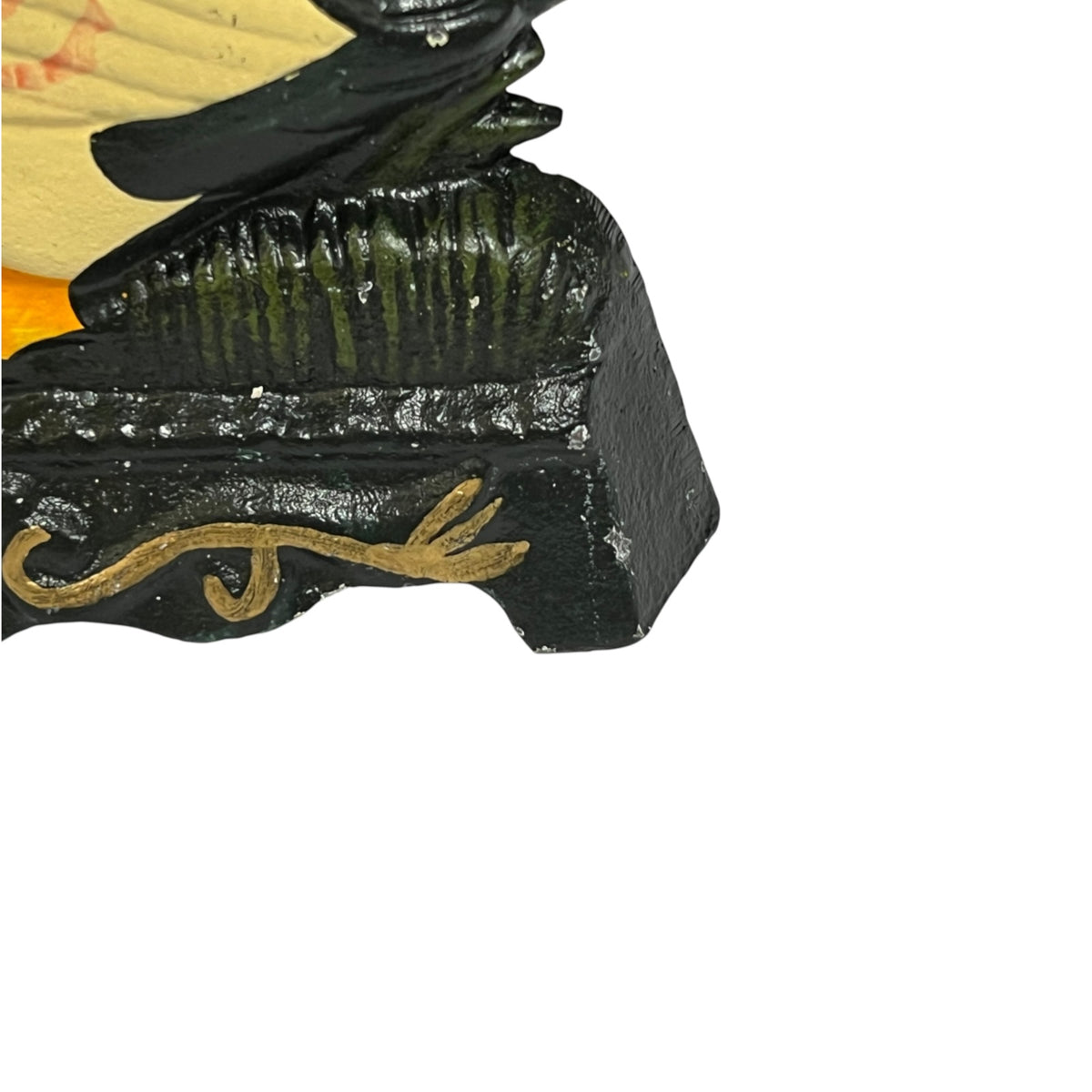 Close-up of a small door stop showing a glossy black base with gold painted script and dark green ridged detailing, alongside yellow and black painted elements, isolated on a white background.