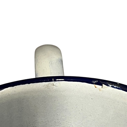 Close-up of the top edge of a white enamel pot with a dark blue rim and a matching white handle, shown against a plain white background.