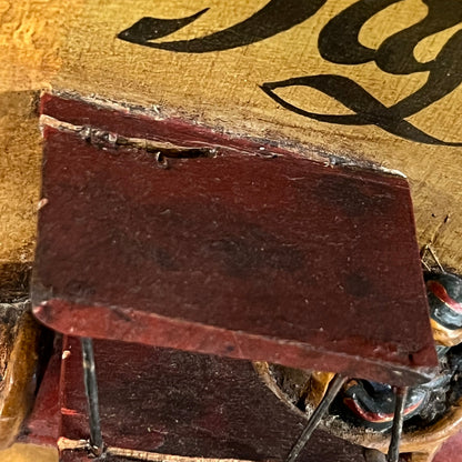 Close-up detail of a vintage wooden picture structure with dark reddish-brown painted wood, black script lettering on a tan surface, and thin metal support rods.