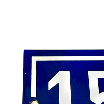 Close-up of a blue rectangular sign or plaque with white lettering and border details, cropped to show part of the characters and a small metal mounting hole near the bottom left.