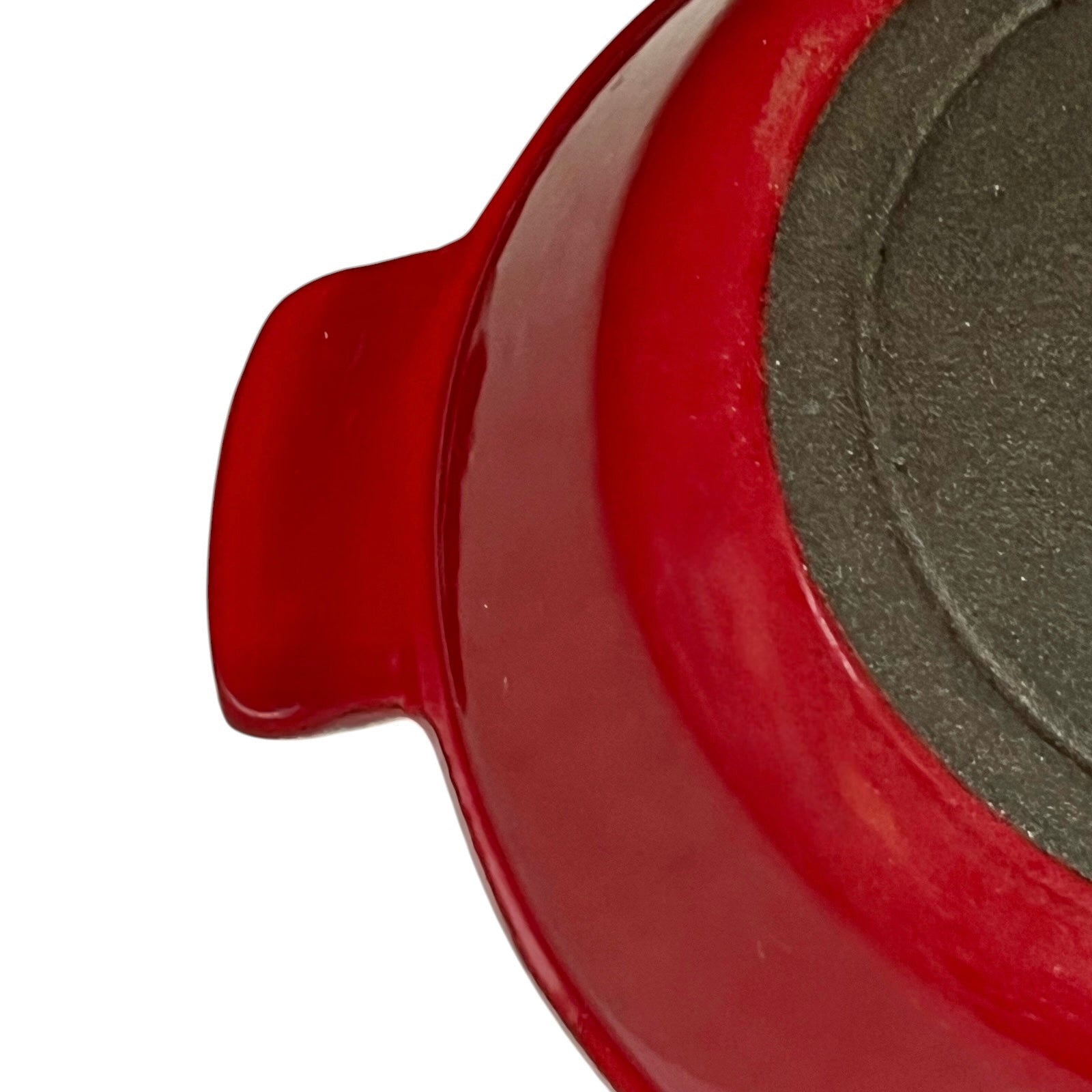 Close-up of a red enameled cast iron skillet showing the side handle and the textured dark gray non-stick interior.