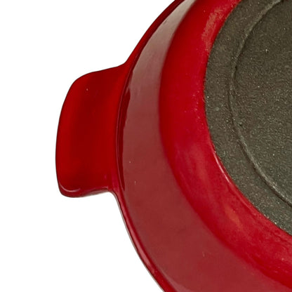 Close-up of a red enameled cast iron skillet showing the side handle and the textured dark gray non-stick interior.