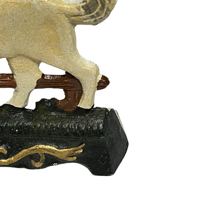 Close-up of a decorative figurine showing part of a cream-colored animal standing on a dark base with gold detailing, isolated on a white background.