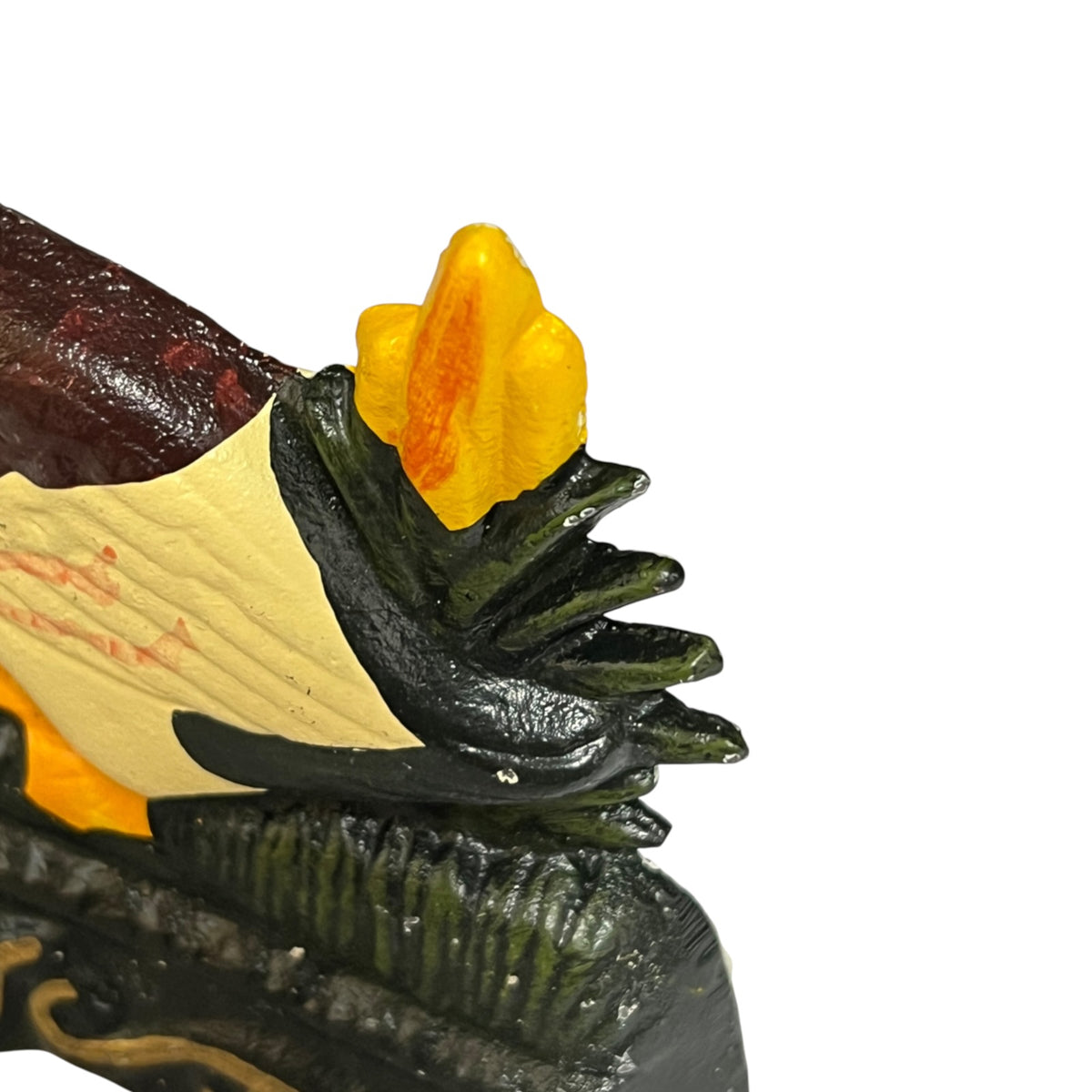 Close-up of a decorative door stop or sculpture showing a dark green leafy form, a cream and red side panel, and a bright yellow-orange flame-like top detail on a plain white background.