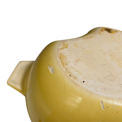 Close-up of the bottom interior of a yellow ceramic baking dish or casserole, showing a light beige glazed base with some wear and chipped areas, on a white background.