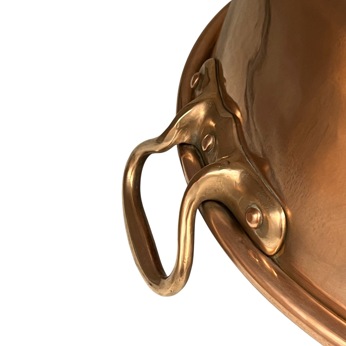 Close-up of a polished copper pot handle attached to the side rim, shown against a plain white background.