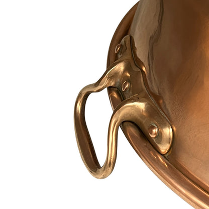 Close-up of a polished copper pot handle attached to the side rim, shown against a plain white background.