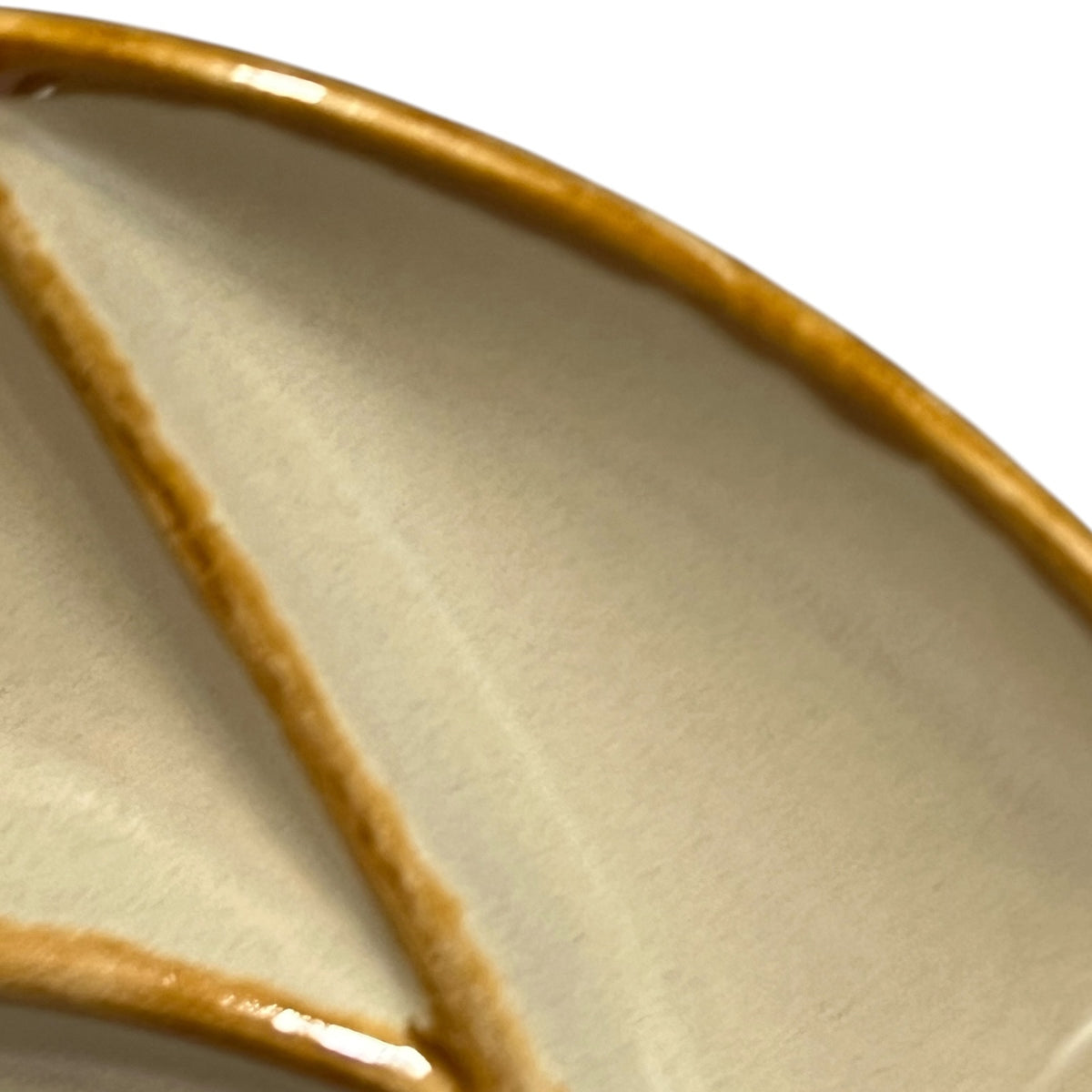 Close-up of a ceramic plate or dish showing a glossy warm brown rim and a cream-colored interior with a subtle leaf-like vein pattern.