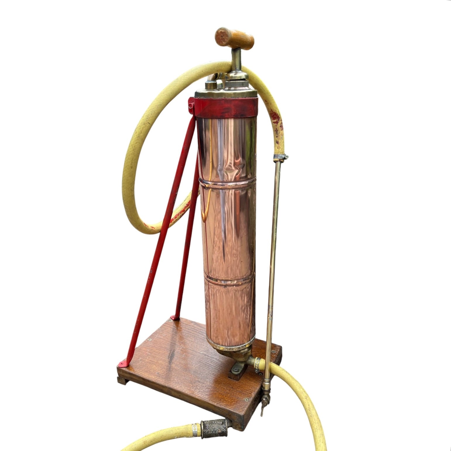 French vintage copper garden sprayer with a yellow hose and nozzle, standing upright on a wooden mount with a red-painted metal bracket. A wooden handle for pumping sits at the top, making it ideal for a vintage garden, all set against a white background.