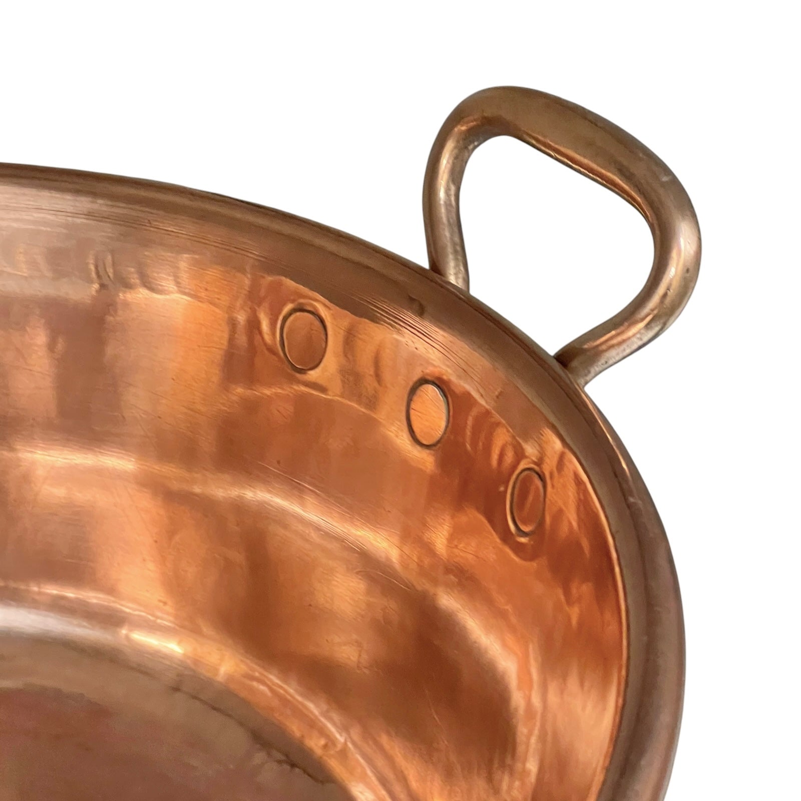 Close-up of a hammered copper pot showing the interior surface and a curved copper handle against a plain white background.