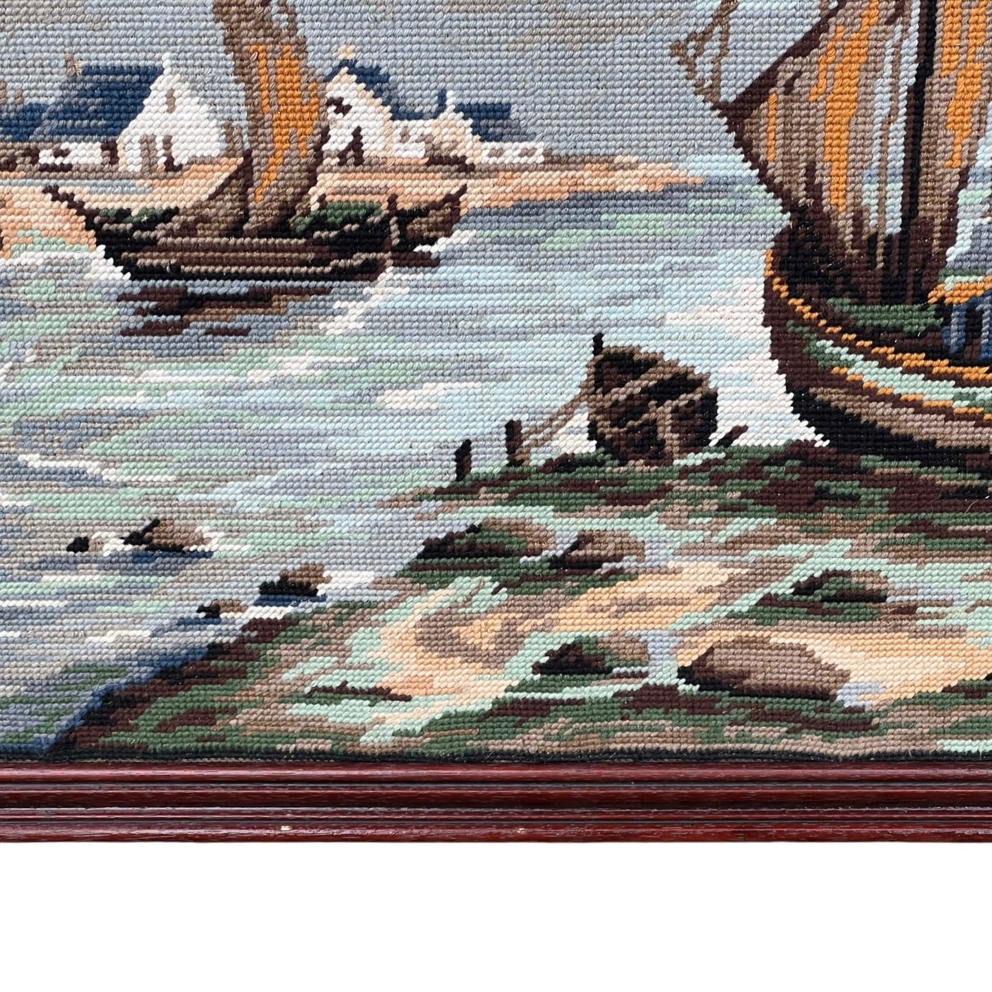 Close up of framed tapestry needlepoint with a coastal scene and wooden frame on a white background