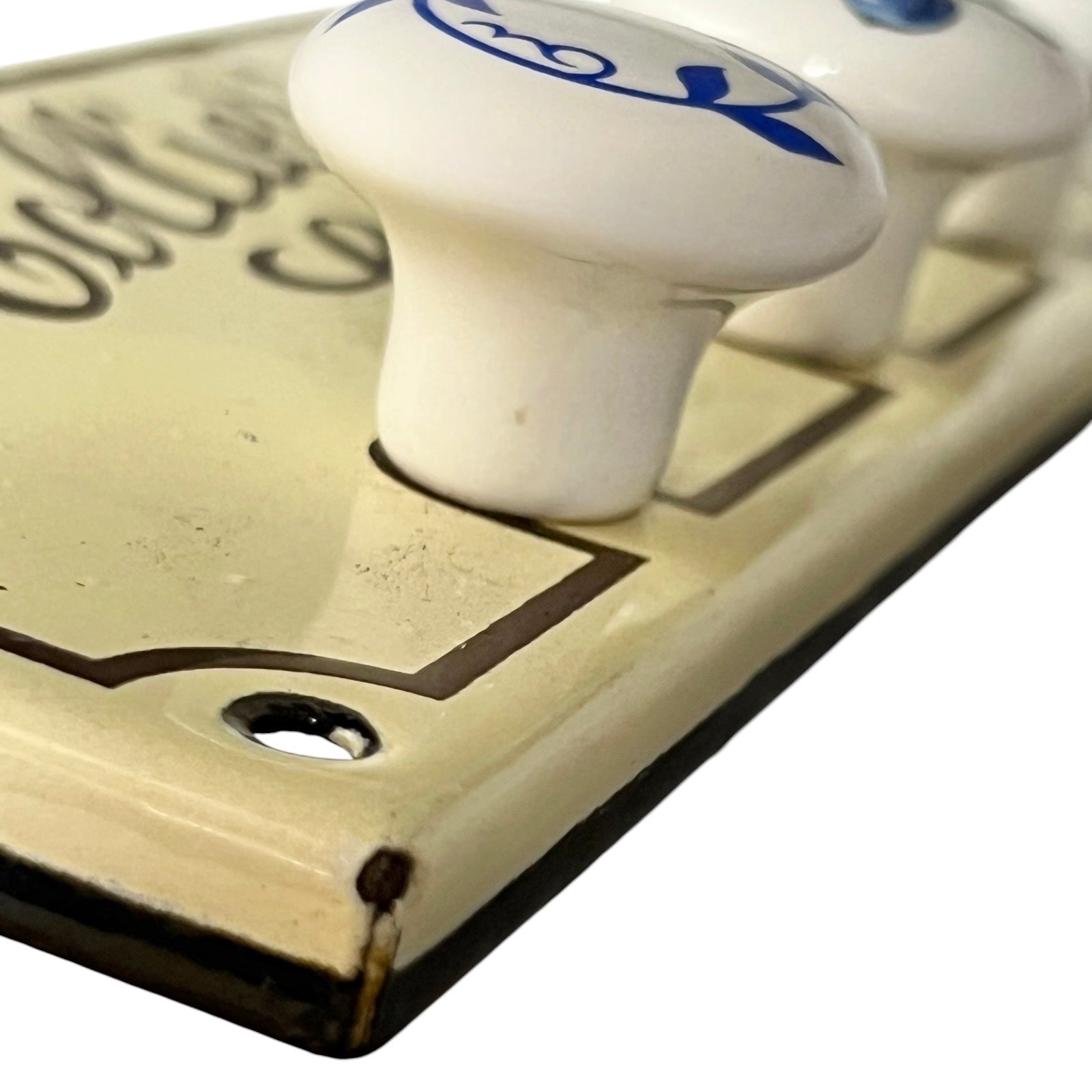 Close-up of a vintage-style cream-coloured plaque with white ceramic knobs featuring blue scrollwork, set against a plain white background.