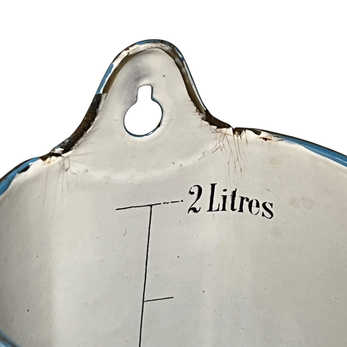 Close-up of the interior of a vintage enamel kitchen utensil, showing a white enamel surface with a blue rim, a hanging loop, and printed black text reading '2 Litres' alongside measurement lines.