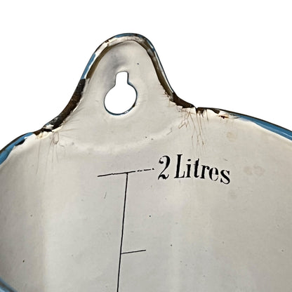 Close-up of the interior of a vintage enamel kitchen utensil, showing a white enamel surface with a blue rim, a hanging loop, and printed black text reading '2 Litres' alongside measurement lines.