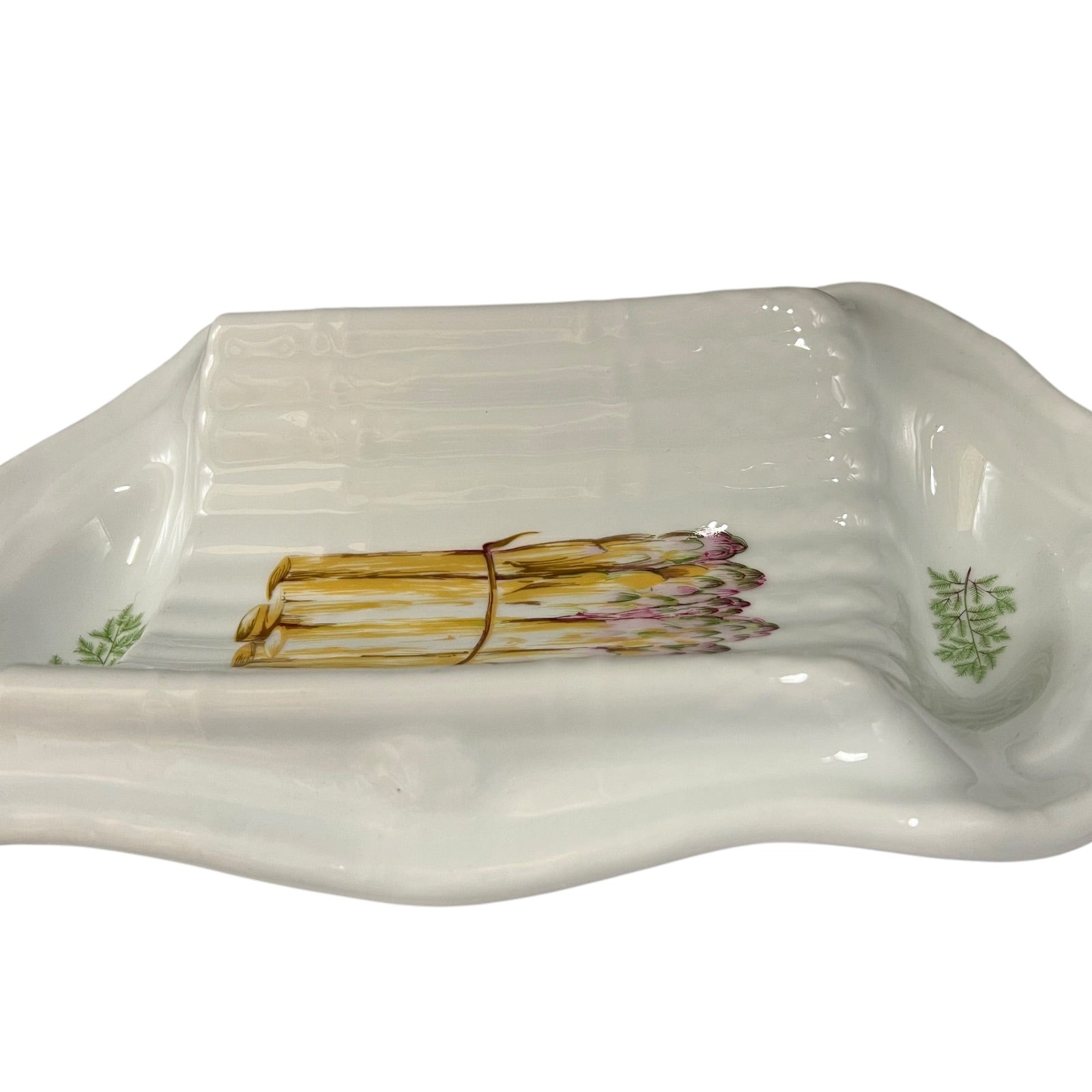 A white ceramic serving tray with a painted illustration of a bundle of asparagus tied with brown string, flanked by small green leaf motifs on the sides.