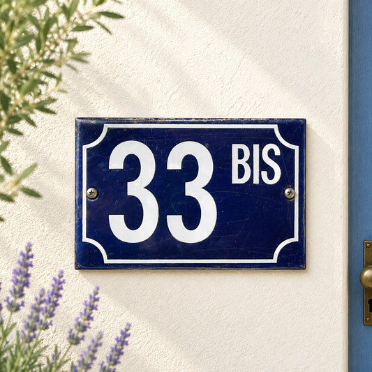 Navy blue house number sign with '33 BIS' on a white wall with lavender plants.