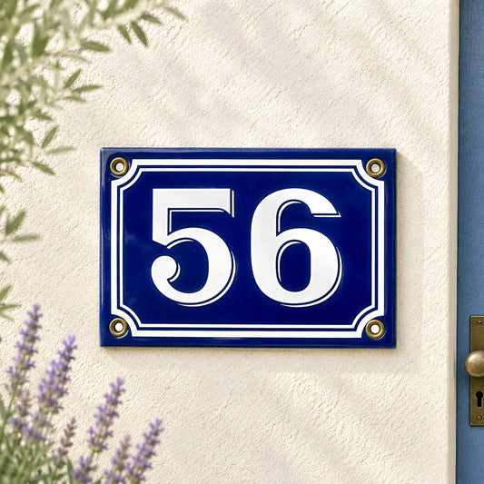 Blue French vintage enamel house number sign with '56' on a white wall.