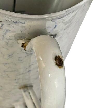 Close-up of a white plant pot with a marbled blue pattern, showing a prominent brown stain on the handle.