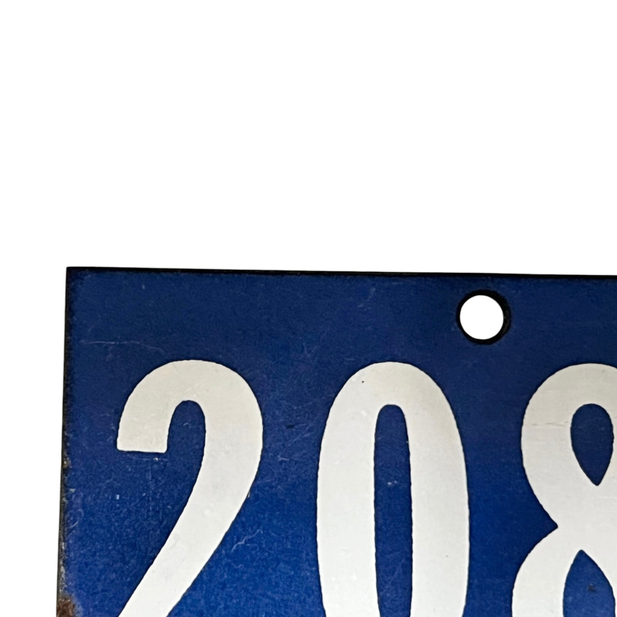 Close-up of a blue rectangular sign or plate with large white numerals '208' and a small round hole near the top right, shown against a white background.