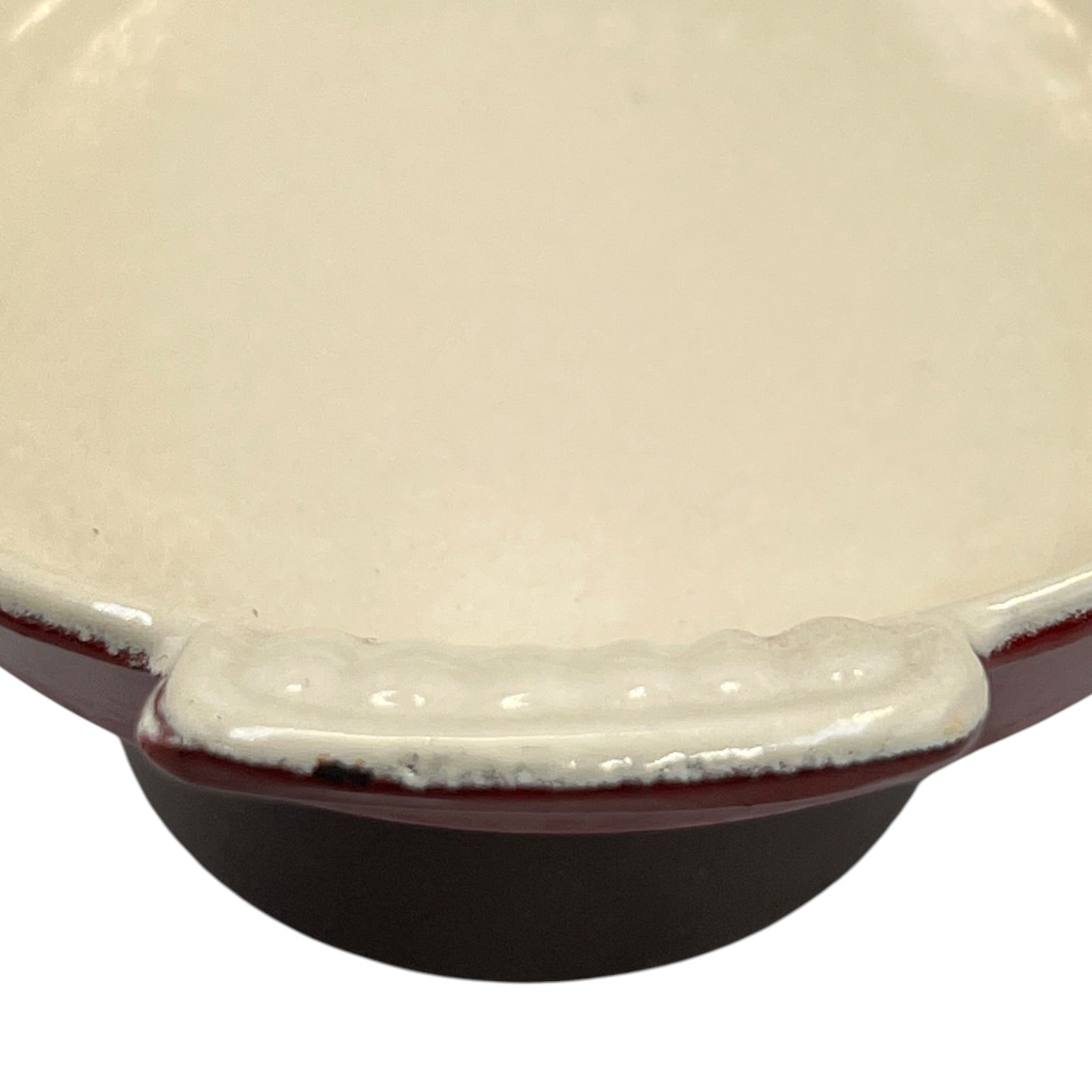 Close-up of a ceramic bowl or dish with a glossy off-white interior, a deep dark brown exterior, and a wavy rim with a reddish-brown glaze, shown on a white background.