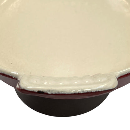 Close-up of a ceramic bowl or dish with a glossy off-white interior, a deep dark brown exterior, and a wavy rim with a reddish-brown glaze, shown on a white background.