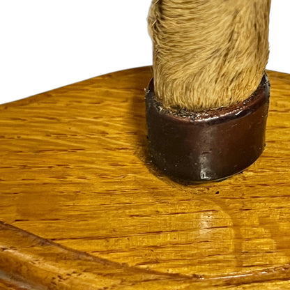Close-up of a wooden display stand with a round polished wood base and a vertical post wrapped in tan fur, set against a plain white background.