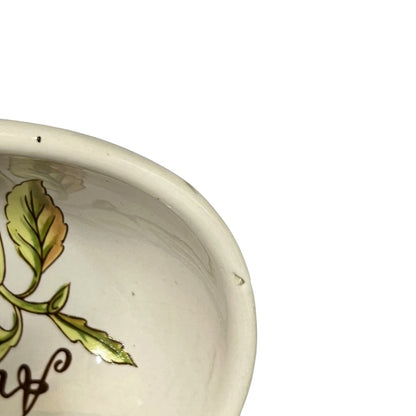 Close-up of a white ceramic bowl showing a painted green leaf design and part of a dark brown script on the inside, against a plain white background.