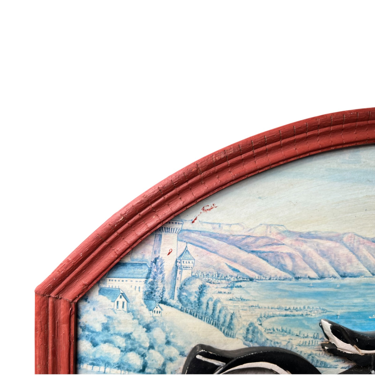 Close-up of an arched framed painting showing a scenic landscape with blue water, mountains, and buildings, bordered by a distressed red frame against a white background.