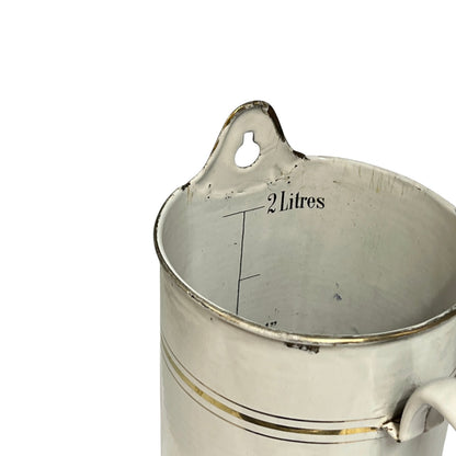 A close-up of a vintage metal measuring jug with a 2 litres capacity, featuring a hanging loop at the rim and measurement markings inside.