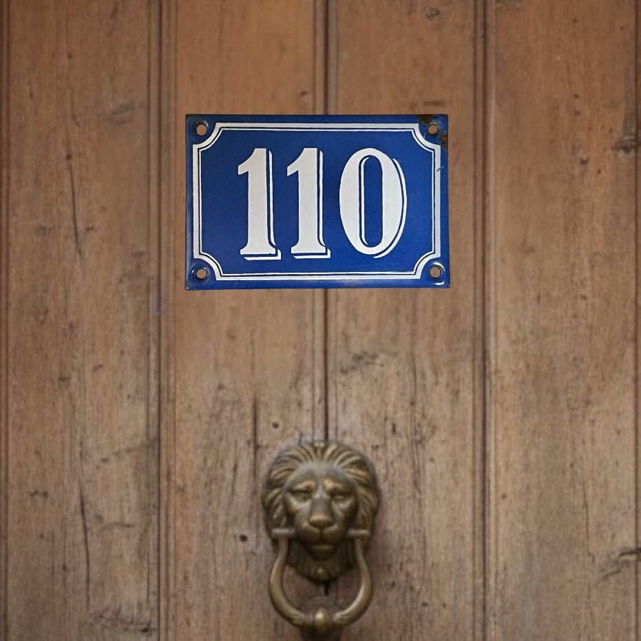 Wooden door with a blue house number sign and lion knocker.