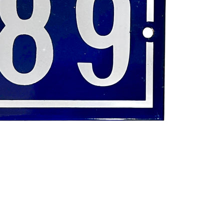 Close-up of a blue and white enamel-style sign showing part of the number sequence '89' with a small mounting hole, photographed against a white background.