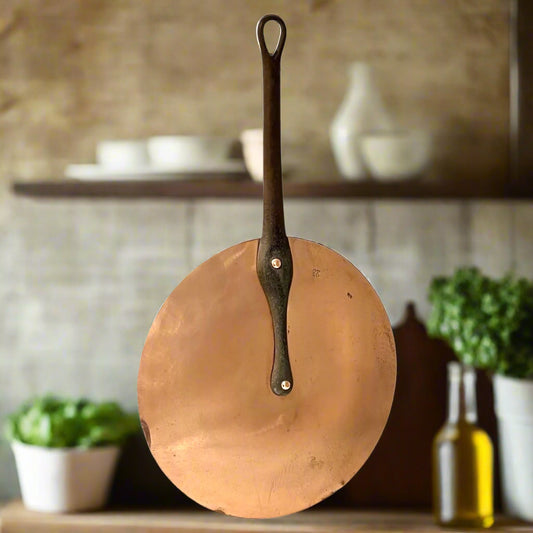 Authentic vintage French copper pan lid with cast iron handle and new tin lining with a blurred rustic kitchen in the background