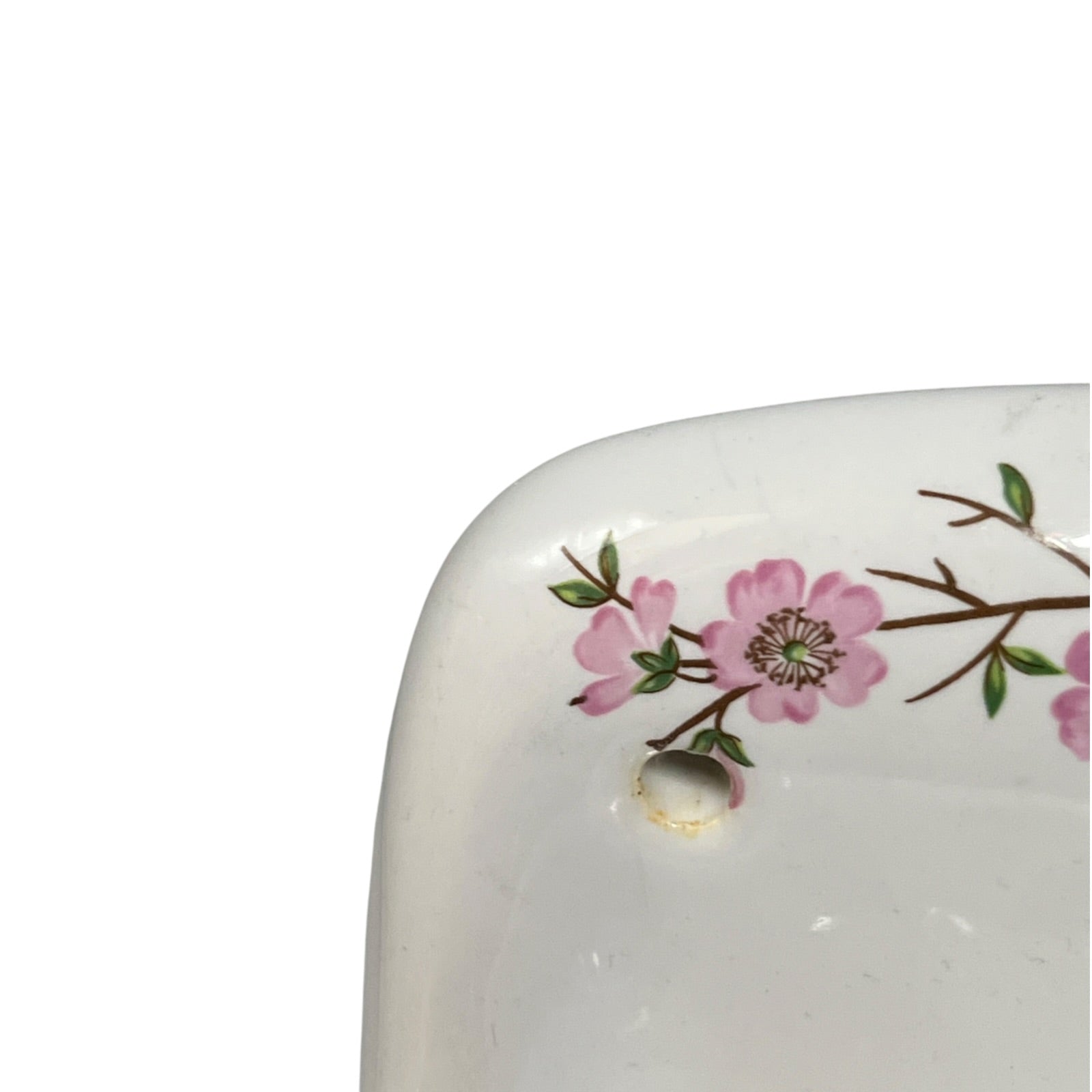 Close-up of a white ceramic dish corner decorated with pink blossoms and green leaves, featuring a small hole near the edge.
