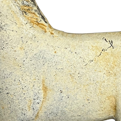 A close-up of a textured bone or antler fragment in pale beige and cream tones with yellowish staining and dark speckles, shown against a white background.
