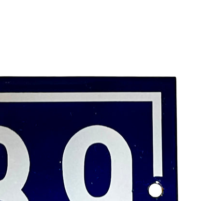 Close-up of a dark blue rectangular sign or plaque with large white numerals and a white border, showing part of the number 189 and a small round hole near the lower right.