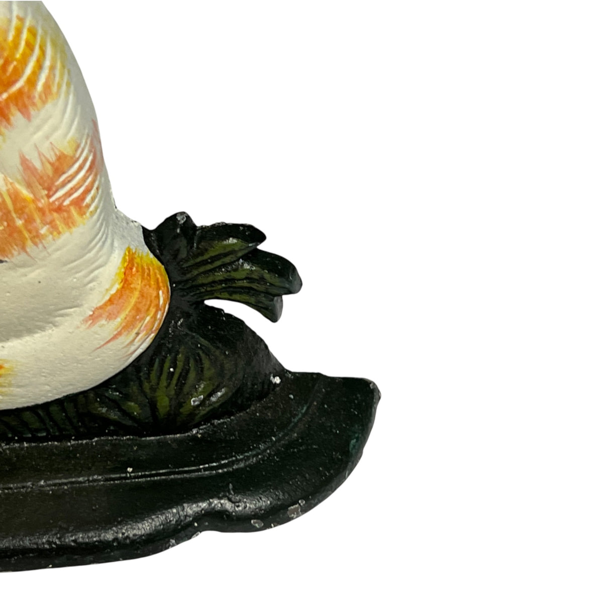 Close-up of a decorative object with a white and orange patterned top section and a dark green to black sculpted base, photographed against a plain white background.