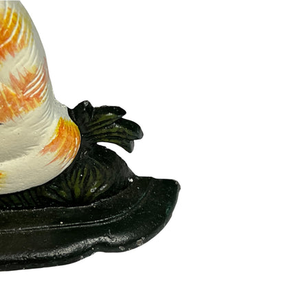 Close-up of a decorative object with a white and orange patterned top section and a dark green to black sculpted base, photographed against a plain white background.