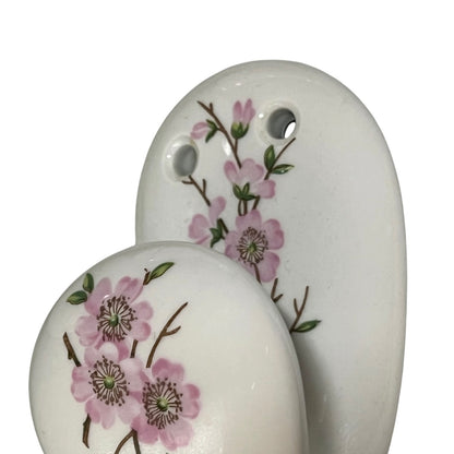 Two white ceramic wall hooks with hand-painted pink plum blossoms and green leaves, shown on a plain white background.