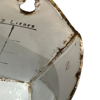 Close-up of a vintage white enamel 2 litres milk jug with rusted brown edges and black printed measurement markings.