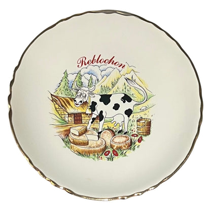 Decorative plate with a cow, mountain, and cabin illustration on a white background