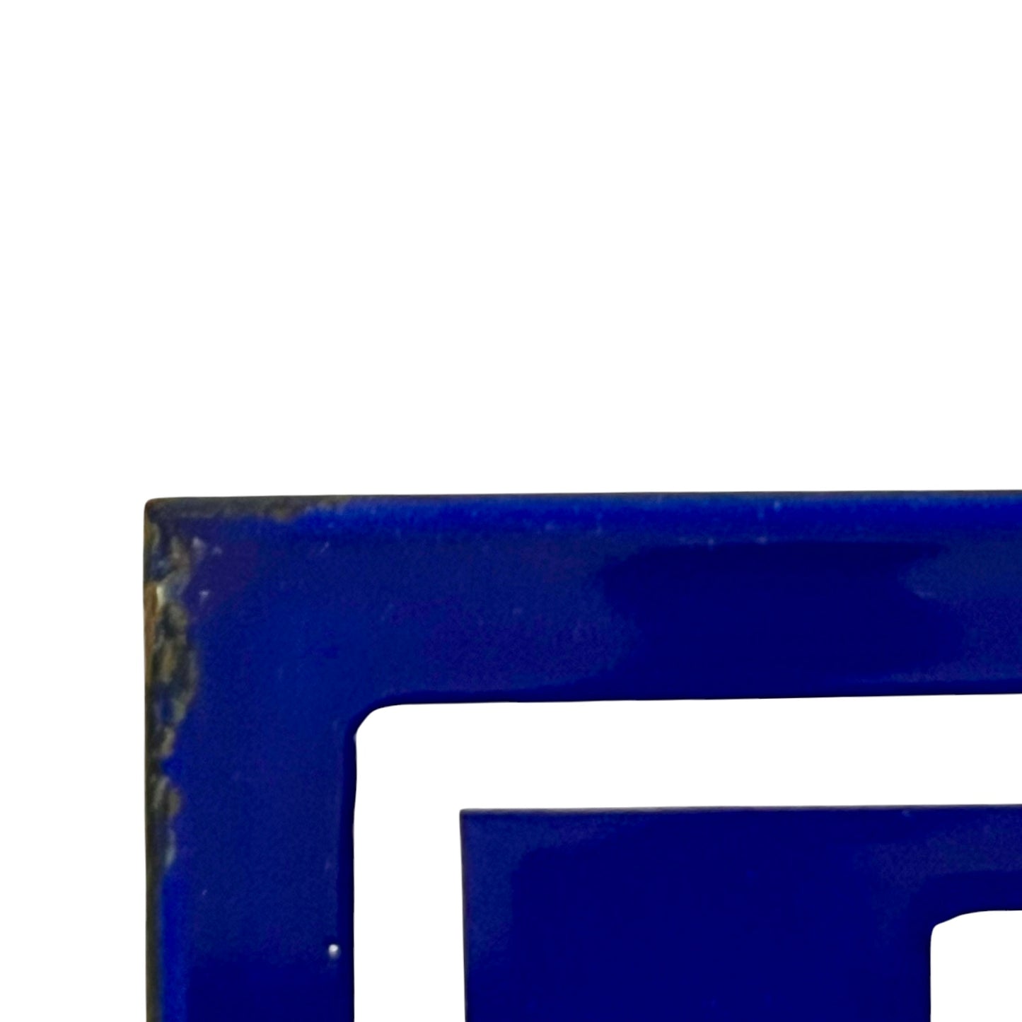 A close-up of a glossy deep blue door number showing a corner with distressed brown patina and a white negative space cutout against a white background.