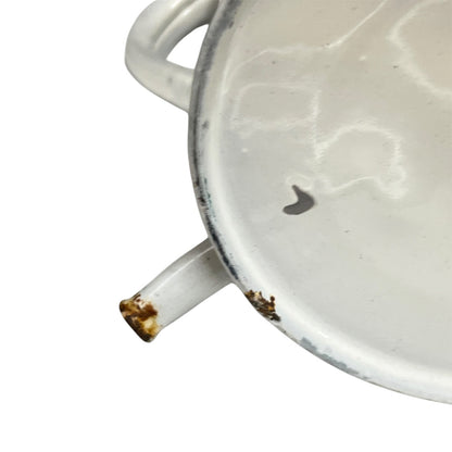 A close-up of a white enamel pot or pan showing the interior surface, a side handle, and a small amount of rust near the spout, isolated on a white background.