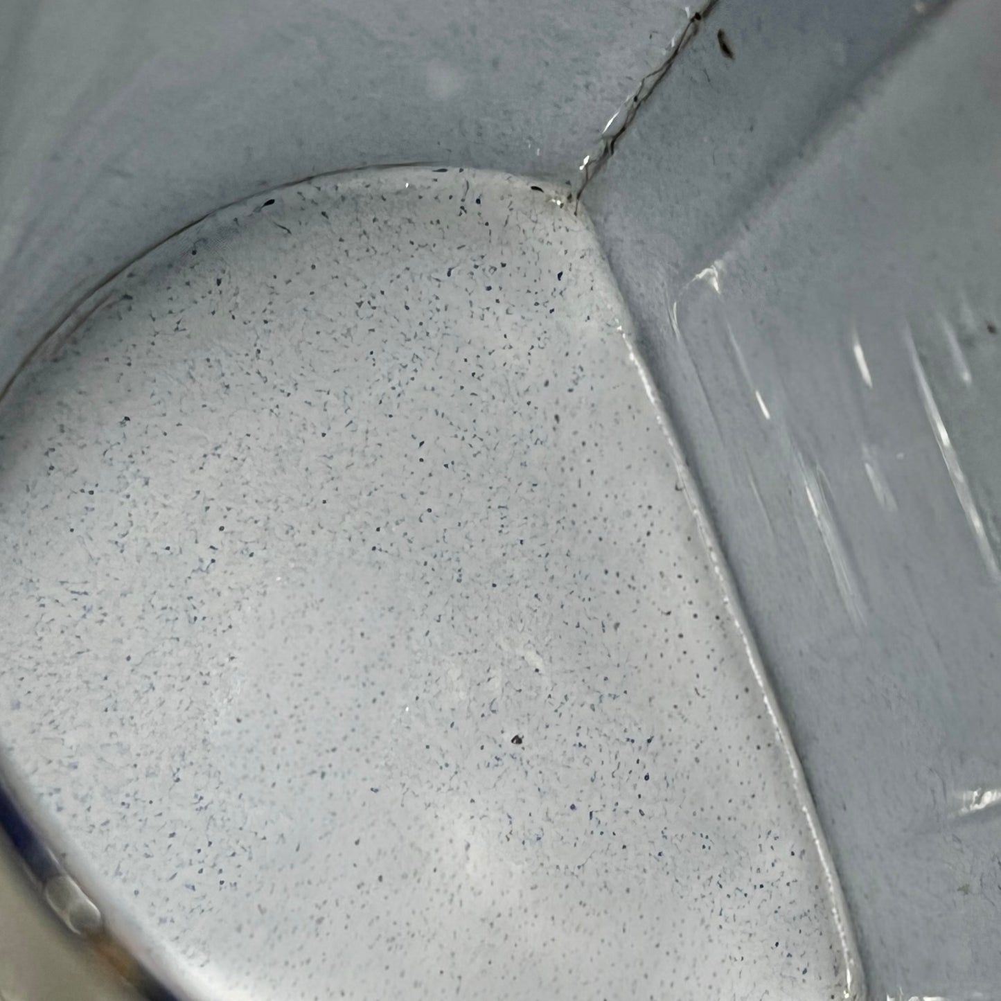 Close-up of the inside of an enamel planter with speckled glaze and blue rim on a white background