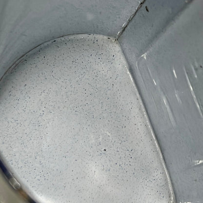 Close-up of the inside of an enamel planter with speckled glaze and blue rim on a white background