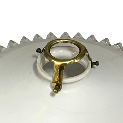 A close-up of a vintage white ceramic lamp shade with a scalloped edge, featuring a central brass metal support ring and a white plastic or acrylic inner collar.