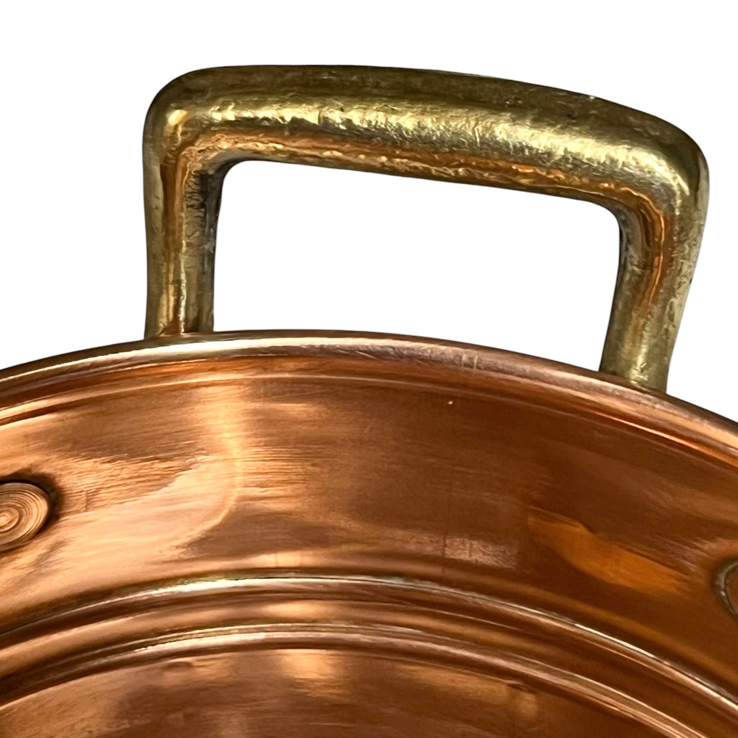 Close-up of a copper pot with a hammered brass handle, showing the reflective metallic surfaces against a plain white background.
