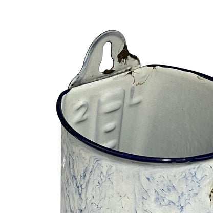 Close-up of a vintage enamel measuring jug with embossed 2L measurement markings, featuring a distressed white and blue marbled pattern, a dark blue rim, and a metal pouring spout on a white background.